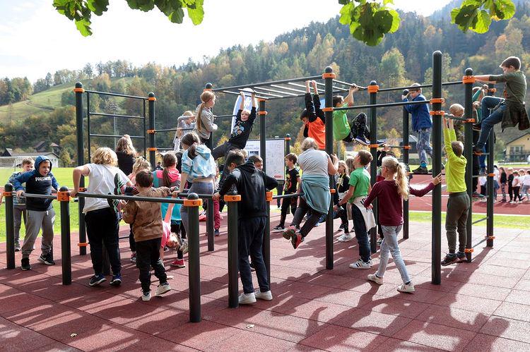 Otroci se igrajo na igralih, nekateri se visijo na vodoravni palici, drugi se plezajo po njej.