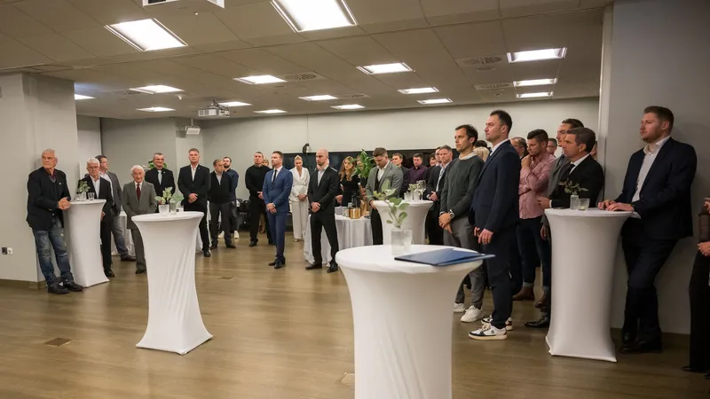 Klub slovenskih olimpijcev, skupina moških in žensk stoji okoli belih miz, nekateri poslušajo, drugi se pogovarjajo.