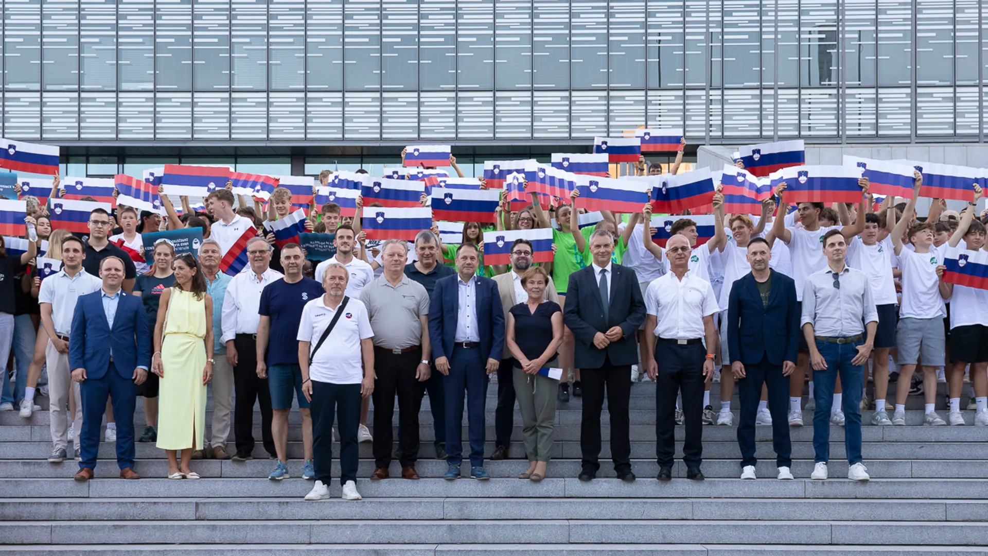 Skupina ljudi stoji na stopnicah in drži slovenske zastave.