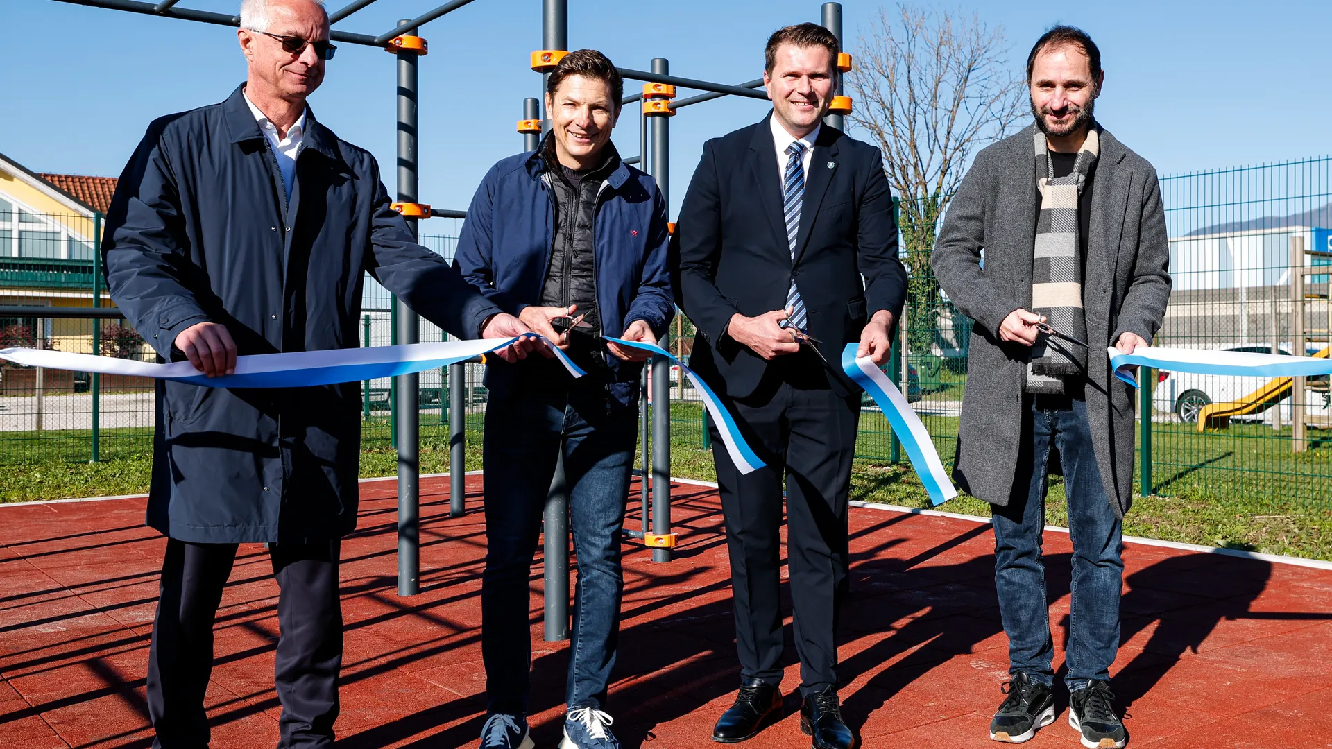 Četverica moških drži trakove, pripravljeni na rezanje ob novem športnem poligonu.