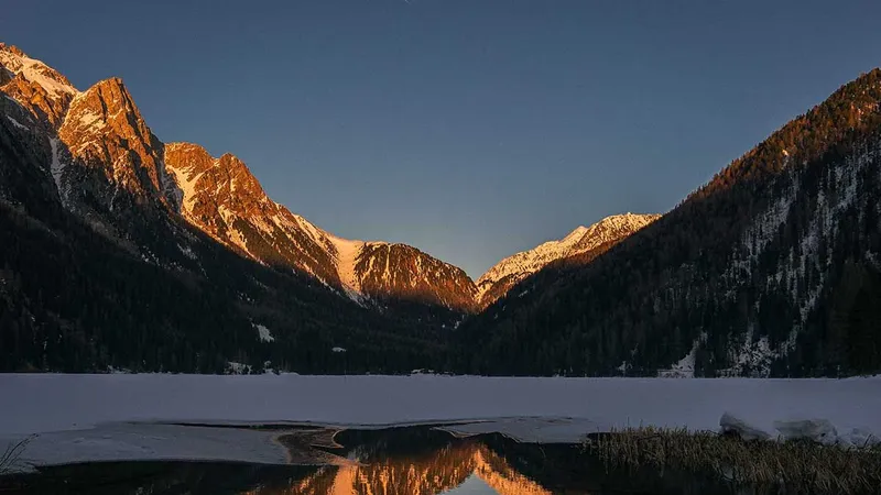 Zasnežene gore se odražajo v mirni vodi jezera, obdanega z naravo.