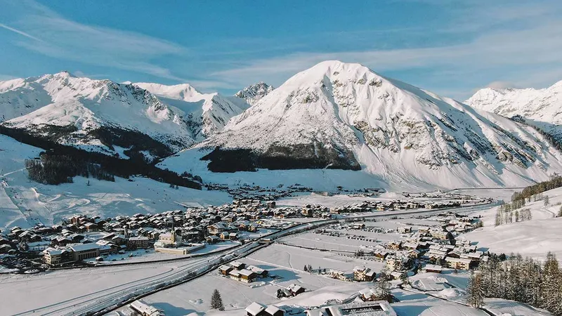 Zasnežena pokrajina z gorami v ozadju in majhnim mestom v dolini.